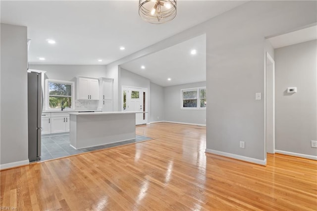 kitchen featuring vaulted ceiling, white cabinets, a kitchen island, light hardwood / wood-style floors, and stainless steel refrigerator