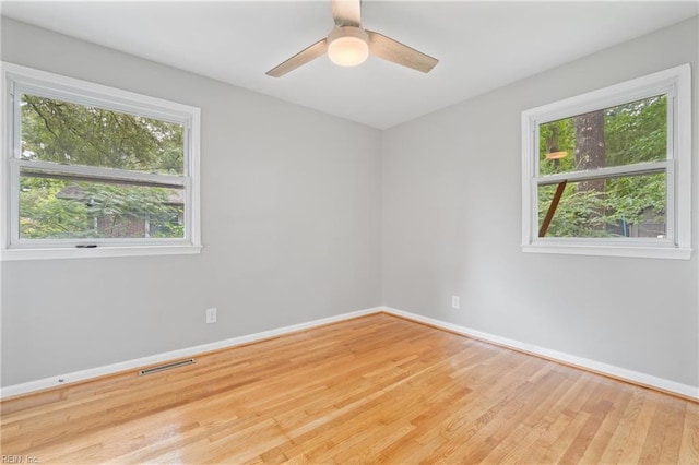 empty room with a healthy amount of sunlight, ceiling fan, and light hardwood / wood-style floors