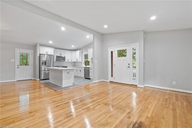 kitchen featuring a center island, vaulted ceiling, white cabinetry, decorative backsplash, and stainless steel appliances