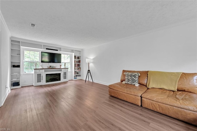 unfurnished living room featuring a textured ceiling, a fireplace, built in features, hardwood / wood-style flooring, and crown molding