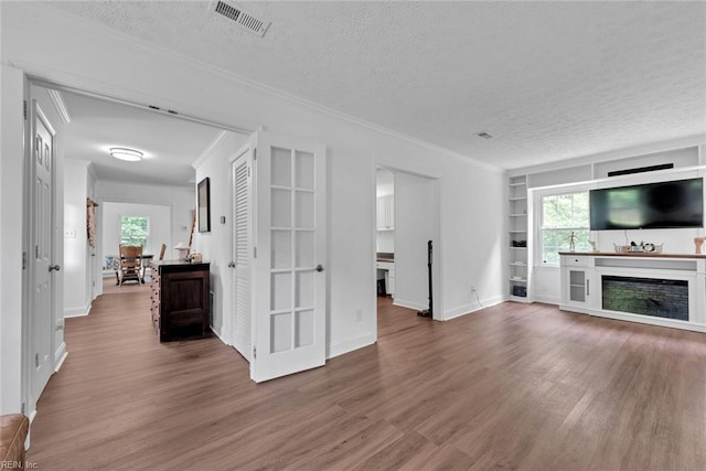 unfurnished living room featuring crown molding, a fireplace, a textured ceiling, hardwood / wood-style flooring, and built in shelves