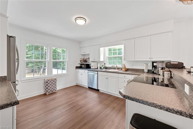 kitchen with white cabinets, stainless steel appliances, sink, kitchen peninsula, and light wood-type flooring