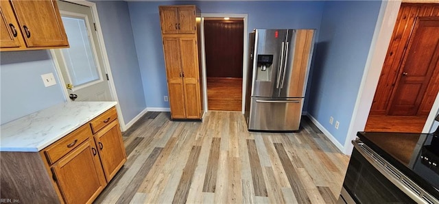 kitchen with light stone counters, stainless steel fridge with ice dispenser, and light hardwood / wood-style flooring