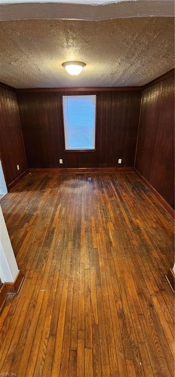 unfurnished room with dark hardwood / wood-style flooring, a textured ceiling, and wooden walls