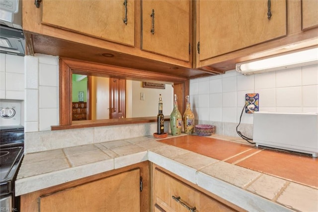 kitchen with decorative backsplash, tile counters, and range