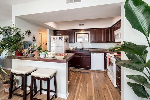 kitchen with dark brown cabinetry, sink, a breakfast bar area, light hardwood / wood-style flooring, and white appliances