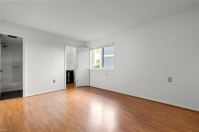 unfurnished bedroom featuring ensuite bathroom, a walk in closet, light wood-type flooring, and a closet