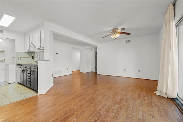 unfurnished living room featuring ceiling fan, a skylight, and light wood-type flooring