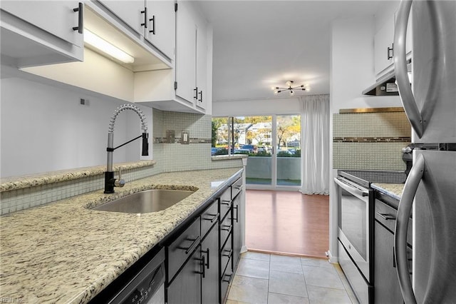 kitchen with sink, white cabinetry, light stone counters, appliances with stainless steel finishes, and backsplash