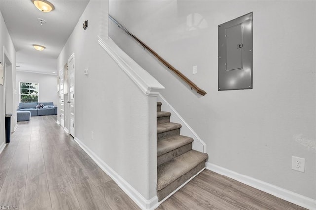 stairway with hardwood / wood-style floors and electric panel