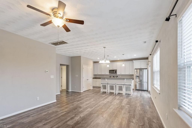 unfurnished living room featuring ceiling fan with notable chandelier and light hardwood / wood-style flooring