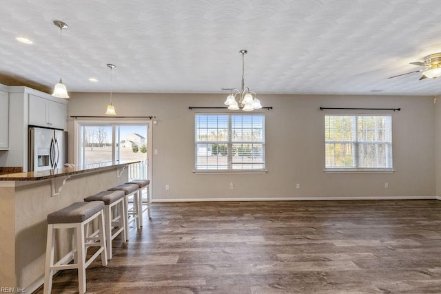 kitchen with white cabinets, a kitchen breakfast bar, dark stone counters, stainless steel refrigerator with ice dispenser, and dark wood-type flooring