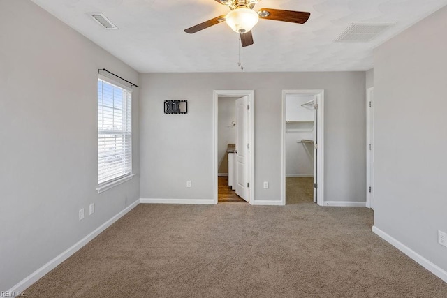 unfurnished bedroom with a spacious closet, a closet, ceiling fan, and carpet