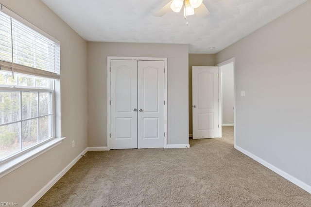 unfurnished bedroom with multiple windows, light colored carpet, ceiling fan, and a closet