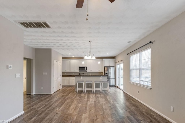 kitchen with a breakfast bar area, white cabinetry, hanging light fixtures, stainless steel appliances, and a center island