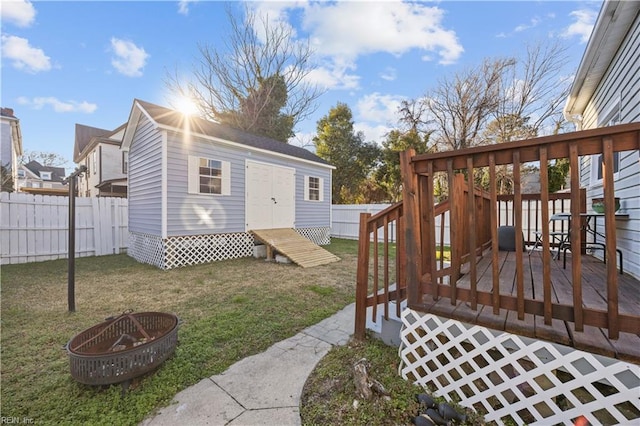 exterior space featuring a wooden deck, an outbuilding, a fire pit, and a lawn