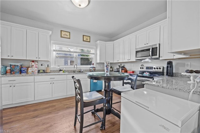 kitchen with sink, white cabinetry, light hardwood / wood-style flooring, stainless steel appliances, and light stone countertops