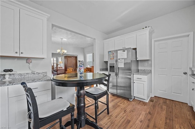 kitchen with stainless steel refrigerator with ice dispenser, light stone countertops, light hardwood / wood-style floors, and white cabinets