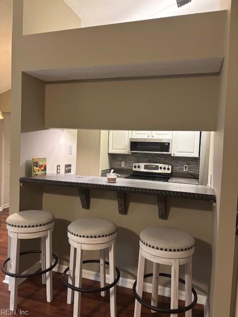 kitchen featuring dark wood-type flooring, a breakfast bar, appliances with stainless steel finishes, white cabinets, and kitchen peninsula