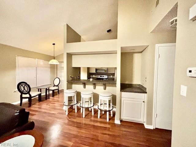 kitchen with dark wood-type flooring, a kitchen breakfast bar, kitchen peninsula, and high vaulted ceiling