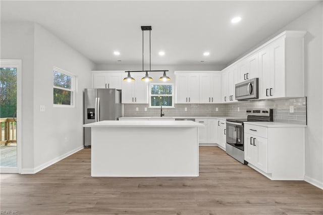 kitchen with white cabinetry, a center island, light wood-type flooring, appliances with stainless steel finishes, and pendant lighting