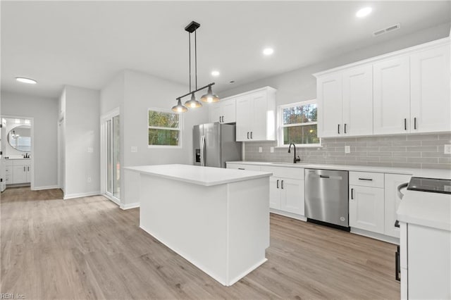 kitchen featuring sink, white cabinetry, stainless steel appliances, a kitchen island, and decorative light fixtures