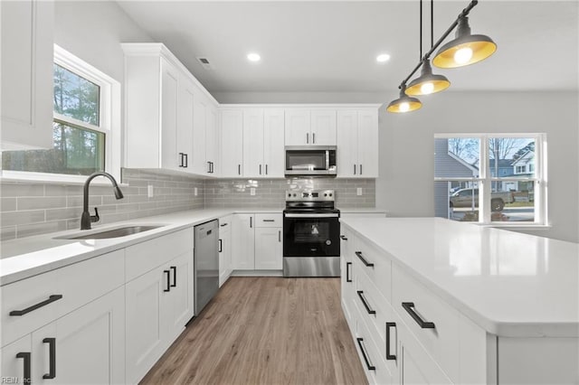 kitchen with stainless steel appliances, white cabinetry, sink, and decorative light fixtures