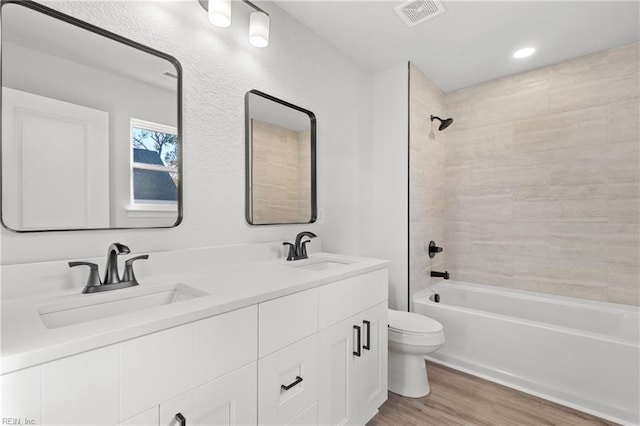 full bathroom featuring hardwood / wood-style flooring, vanity, tiled shower / bath combo, and toilet