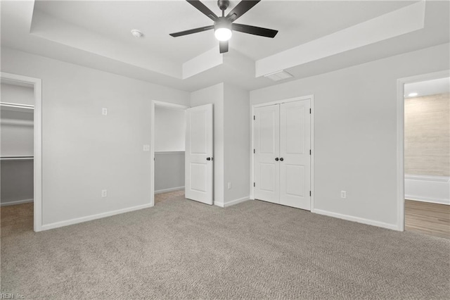 unfurnished bedroom with a raised ceiling, light carpet, and ceiling fan