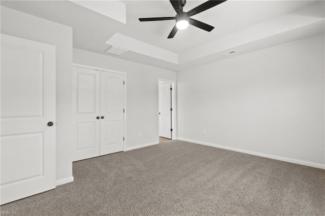 unfurnished bedroom with ceiling fan, a tray ceiling, a closet, and carpet