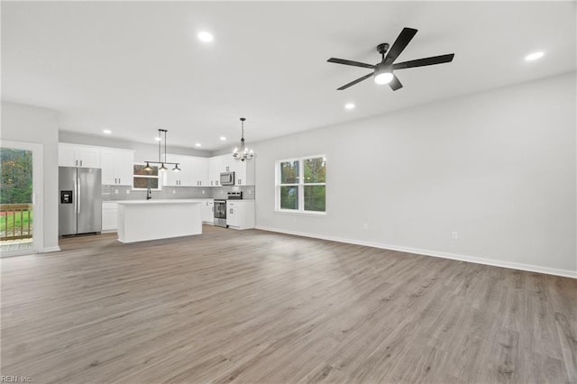 unfurnished living room featuring ceiling fan with notable chandelier and light hardwood / wood-style floors