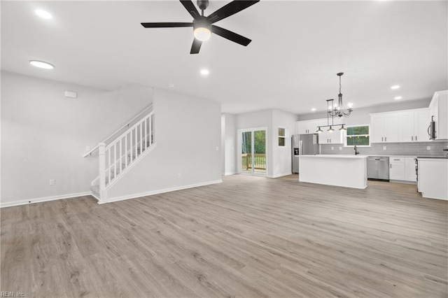 unfurnished living room with sink, ceiling fan with notable chandelier, and light hardwood / wood-style floors