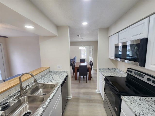 kitchen featuring stainless steel appliances, white cabinetry, light stone countertops, and sink