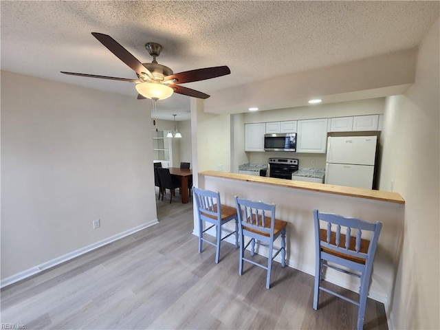 kitchen with a breakfast bar, white cabinets, white fridge, electric range, and kitchen peninsula