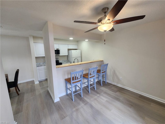 kitchen featuring a kitchen breakfast bar, white refrigerator, light hardwood / wood-style floors, white cabinets, and kitchen peninsula