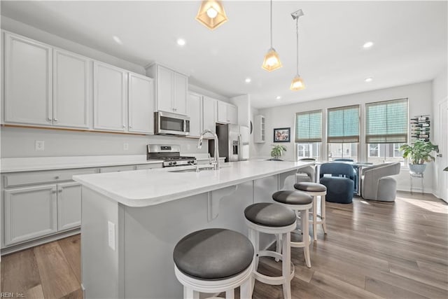 kitchen with a kitchen island with sink, sink, decorative light fixtures, and appliances with stainless steel finishes