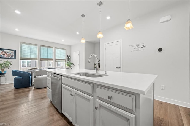 kitchen with pendant lighting, sink, dishwasher, hardwood / wood-style floors, and a center island with sink