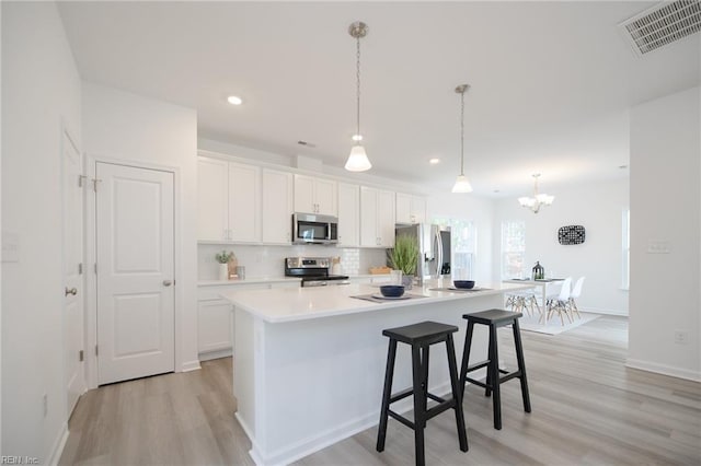 kitchen with white cabinetry, appliances with stainless steel finishes, a kitchen island with sink, and pendant lighting