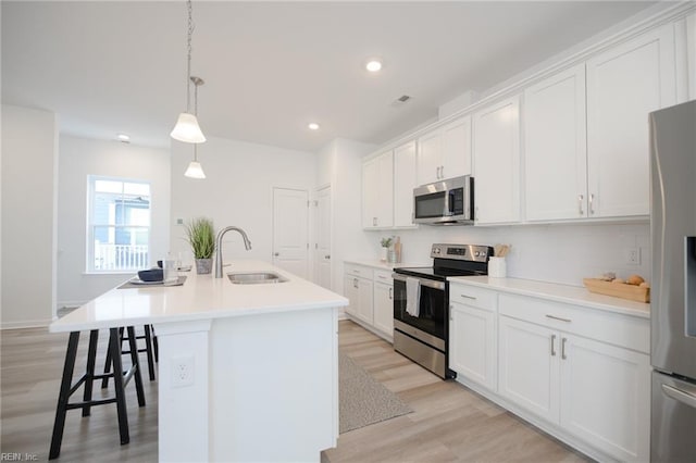 kitchen featuring appliances with stainless steel finishes, pendant lighting, white cabinetry, an island with sink, and sink