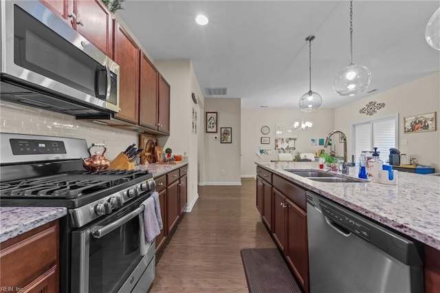 kitchen featuring dark wood-type flooring, sink, light stone counters, pendant lighting, and stainless steel appliances