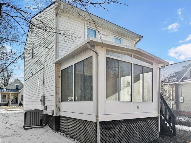 snow covered property featuring central AC unit and a sunroom