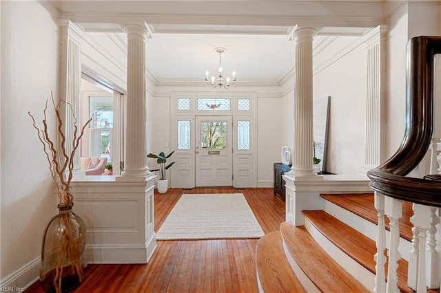 entryway featuring ornate columns, ornamental molding, a notable chandelier, and light hardwood / wood-style flooring