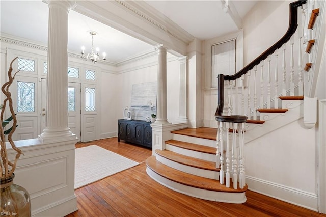 foyer entrance featuring a notable chandelier, ornamental molding, light hardwood / wood-style floors, and ornate columns