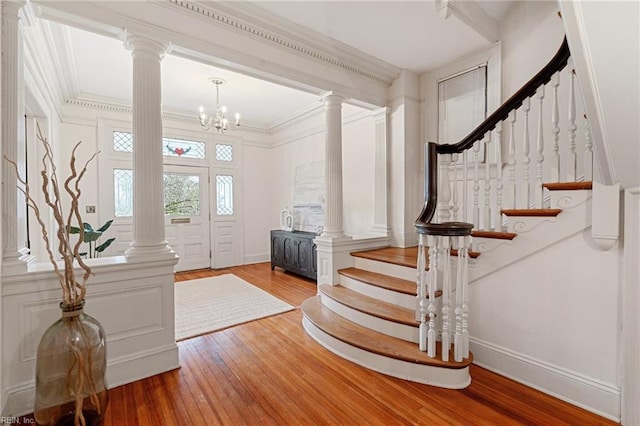 foyer entrance with an inviting chandelier, ornamental molding, wood-type flooring, and decorative columns