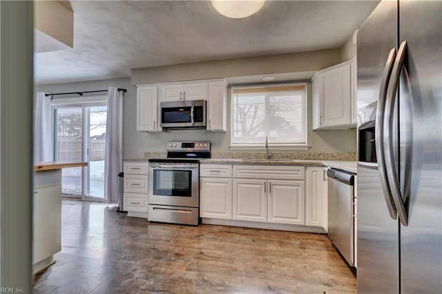 kitchen featuring appliances with stainless steel finishes, white cabinetry, sink, light stone counters, and light hardwood / wood-style floors