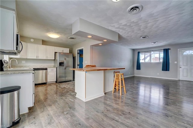 kitchen featuring a kitchen bar, sink, white cabinetry, stainless steel appliances, and hardwood / wood-style floors