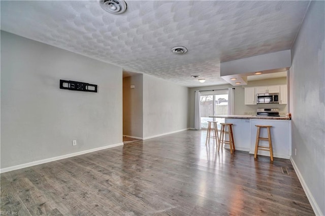 interior space featuring appliances with stainless steel finishes, a breakfast bar area, white cabinets, dark hardwood / wood-style flooring, and kitchen peninsula