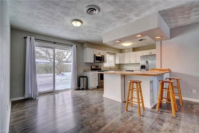 kitchen featuring a breakfast bar, white cabinetry, kitchen peninsula, stainless steel appliances, and dark wood-type flooring