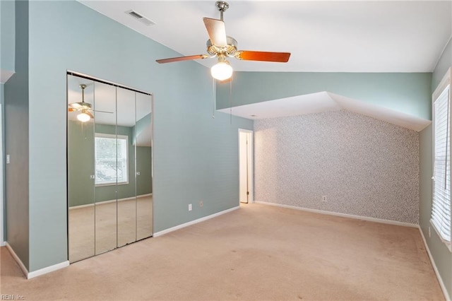 unfurnished bedroom featuring ceiling fan, light colored carpet, vaulted ceiling, and a closet