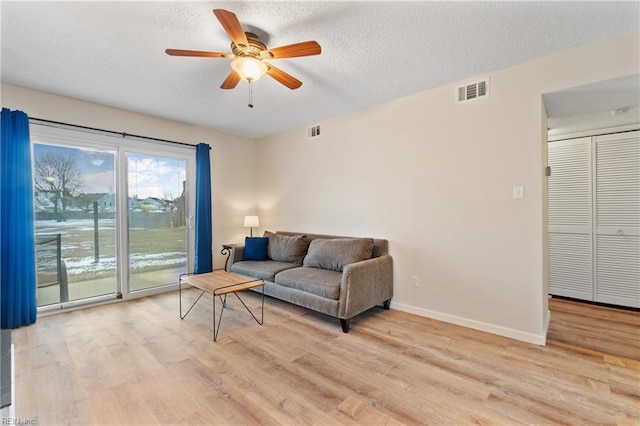 living room featuring ceiling fan, a textured ceiling, and light hardwood / wood-style floors